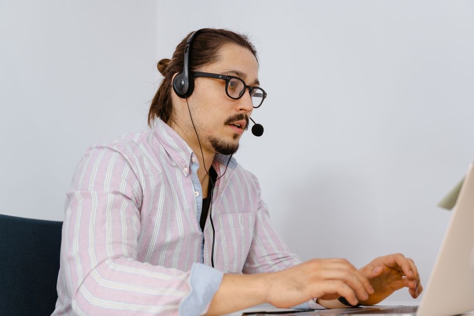 Um jovem em uma camisa listrada trabalha em um laptop, usando um fone de ouvido para suporte ao cliente.