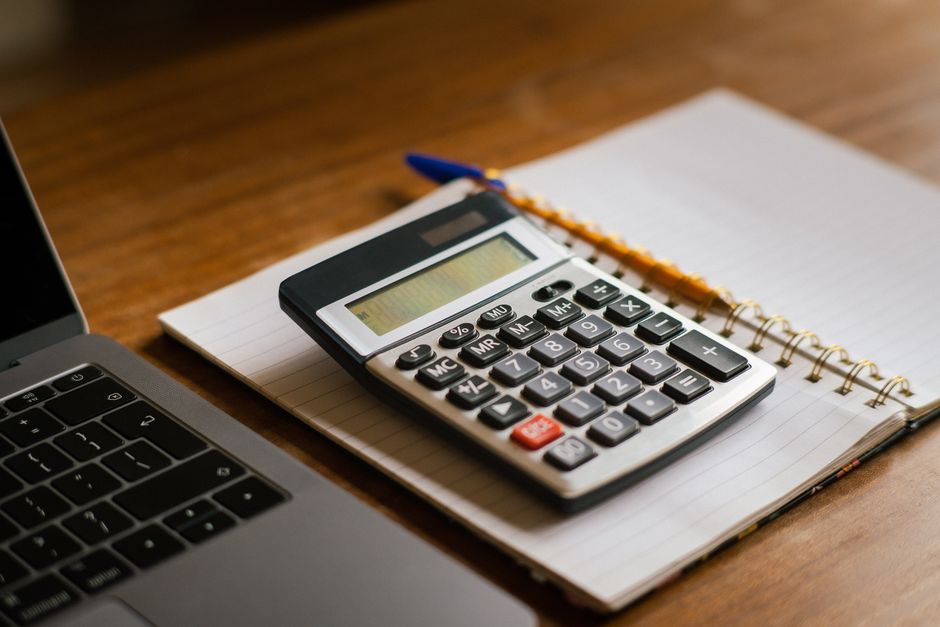 Calculadora e laptop aberto sobre uma mesa de madeira, ideal para tarefas financeiras ou contábeis.