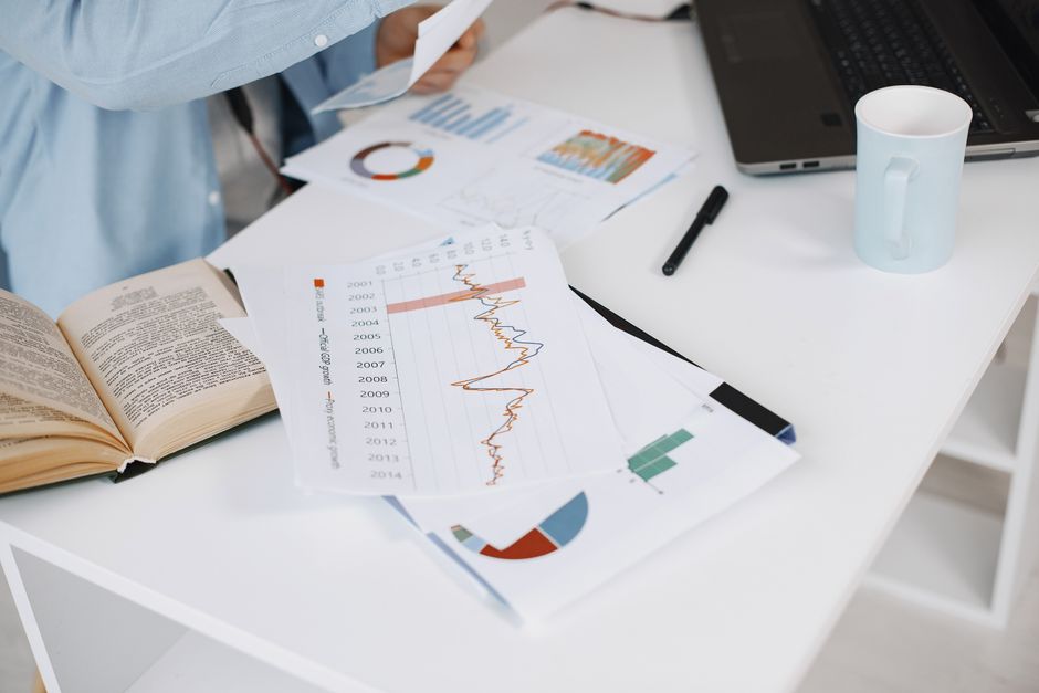 Espaço de trabalho de escritório com gráficos de dados, livro e laptop em uma mesa branca.