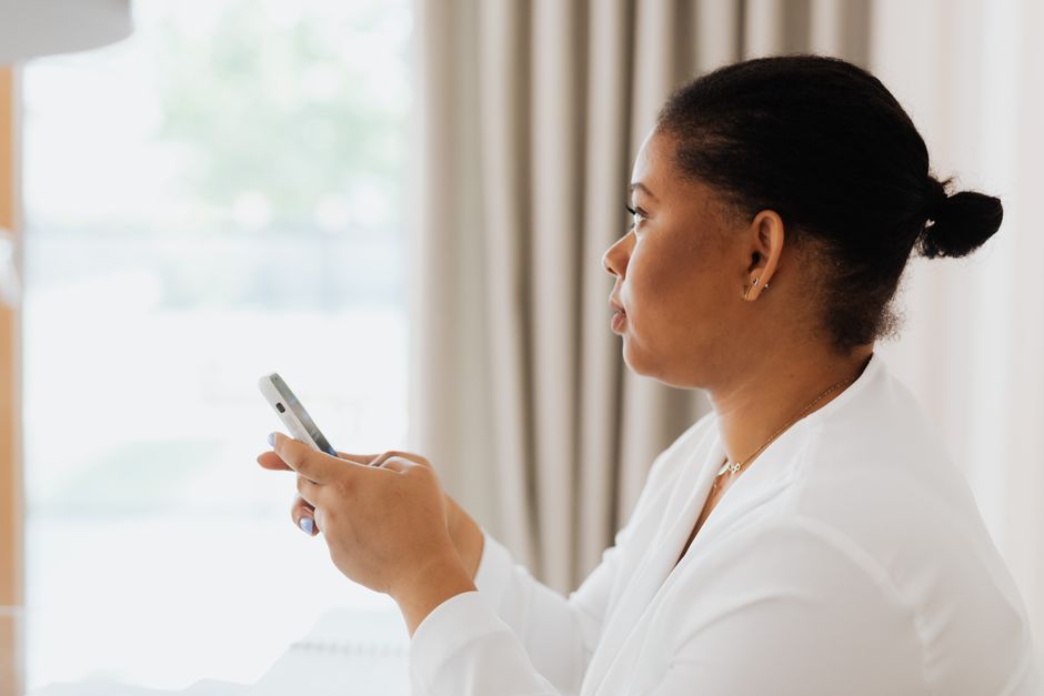 Uma mulher profissional utilizando seu smartphone dentro de casa, focada no trabalho.
