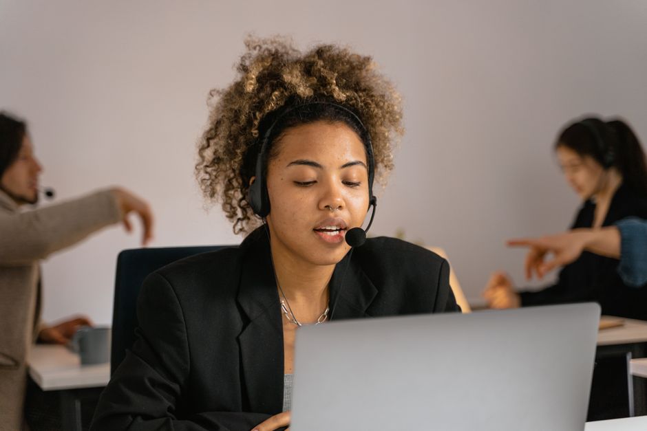 Agente de suporte ao cliente com fone de ouvido trabalhando no laptop no escritório.