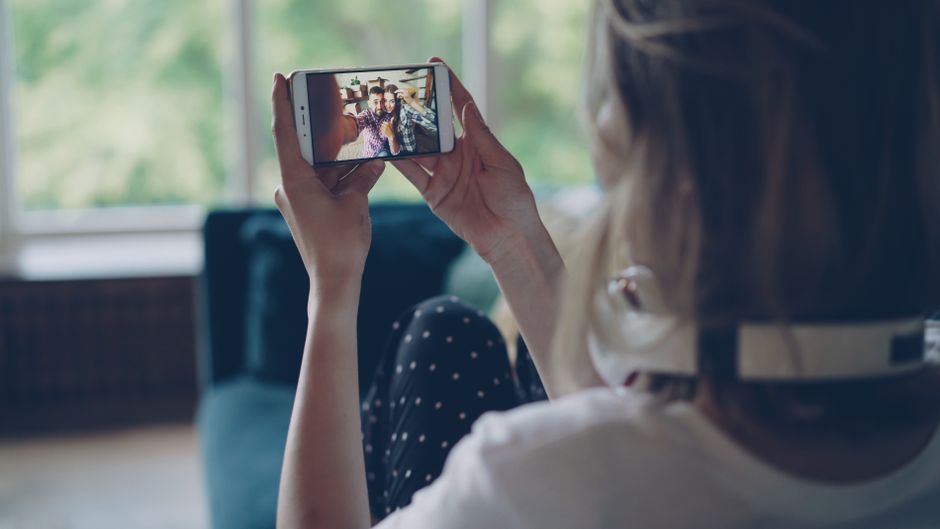 Mulher sentada no sofá, capturando selfie com o telefone dentro de casa, usando fones de ouvido.