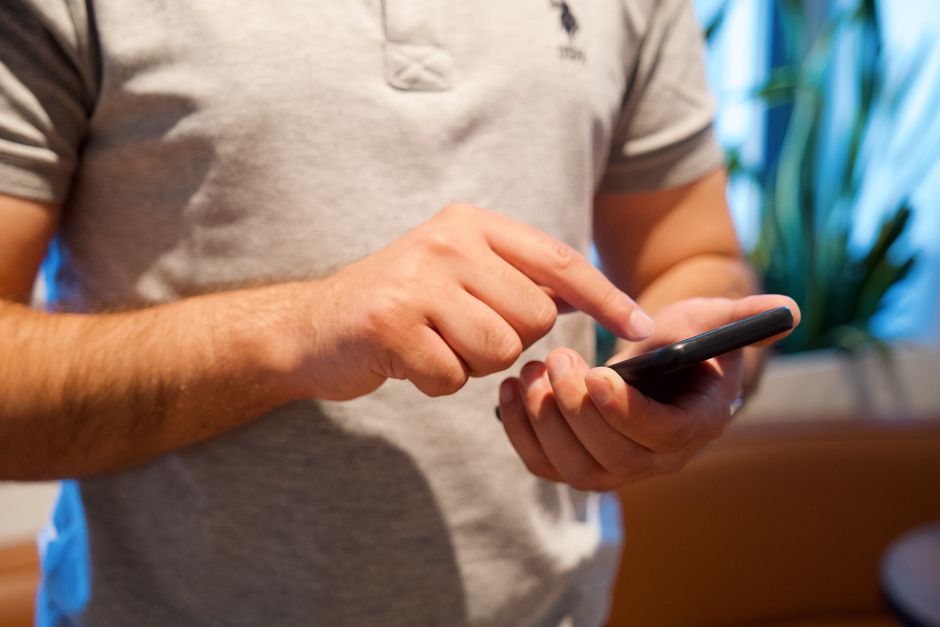Homem adulto usando smartphone em um ambiente interno iluminado, focando no dispositivo e na interação.