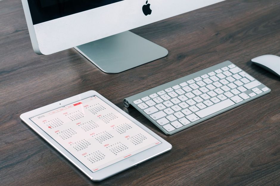 Um ambiente de escritório moderno e elegante com um iMac, iPad com calendário, teclado e mouse.