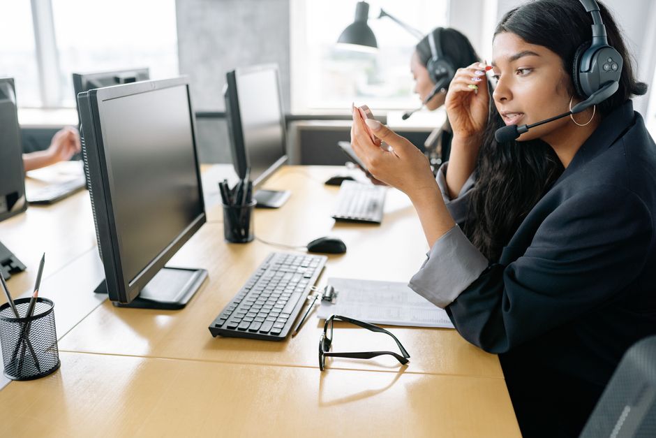 Mulher sul-asiática fornecendo suporte ao cliente em um ambiente de escritório moderno, equipada com um headset.