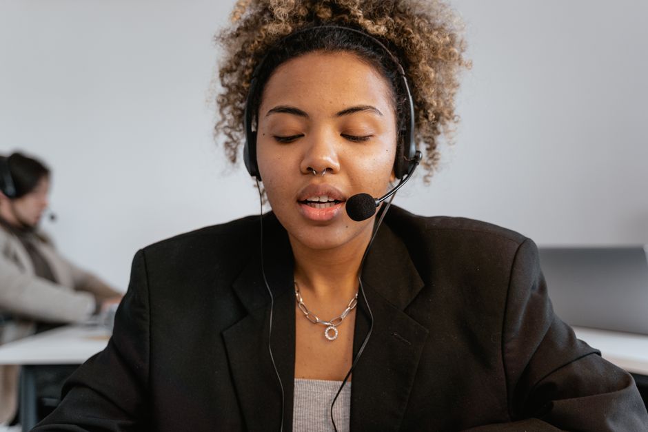 Close-up de uma agente de call center com cabelo cacheado e fones de ouvido em um ambiente de escritório profissional.