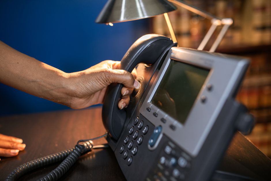 Uma imagem de close-up de uma mão pegando um fone de um telefone de escritório, enfatizando o uso de dispositivos de comunicação.