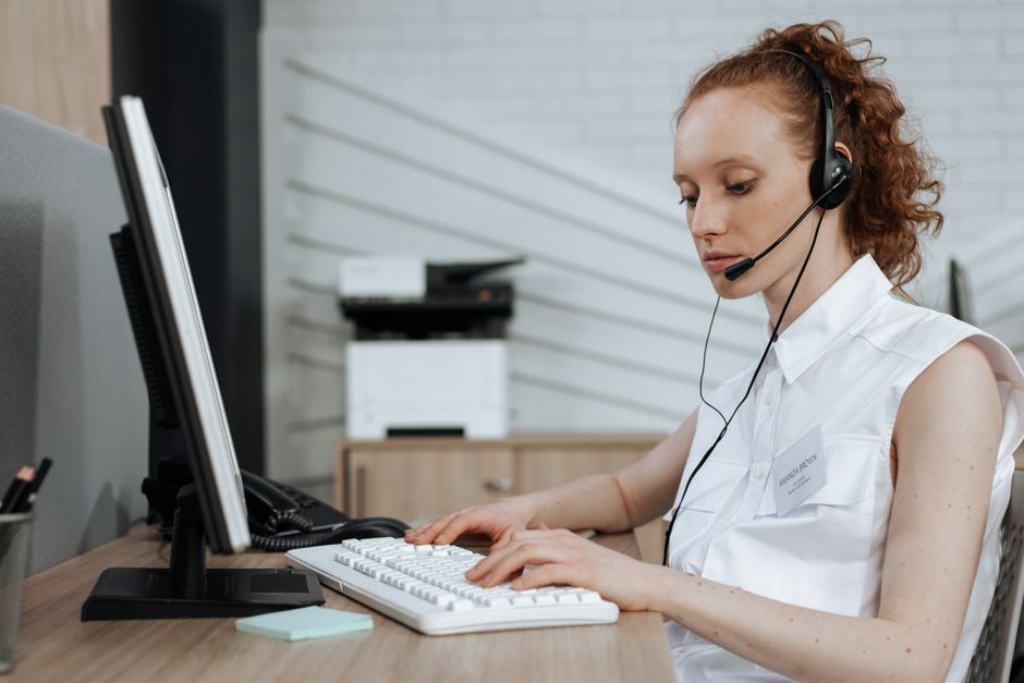 Uma agente de call center digitando em um teclado enquanto usa um fone de ouvido em sua mesa.