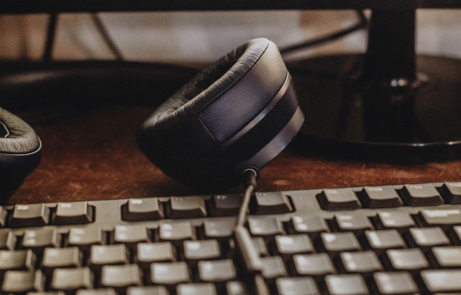 Uma imagem em close de fones de ouvido e teclado em uma mesa de madeira. Ideal para temas de tecnologia e espaço de trabalho.